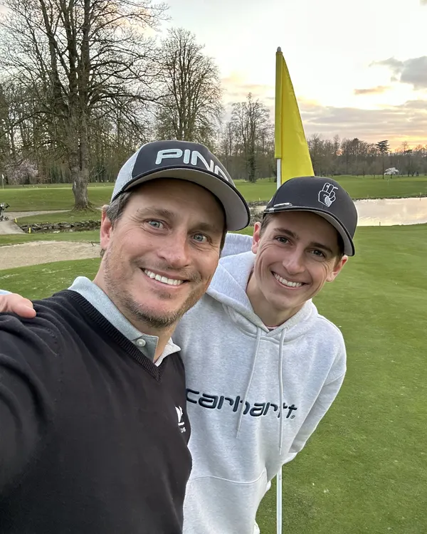 Charles et son père Nicolas, souriants, près du drapeau d’un green au coucher du soleil